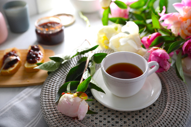 Photo of Beautiful peonies and cup of tea on table
