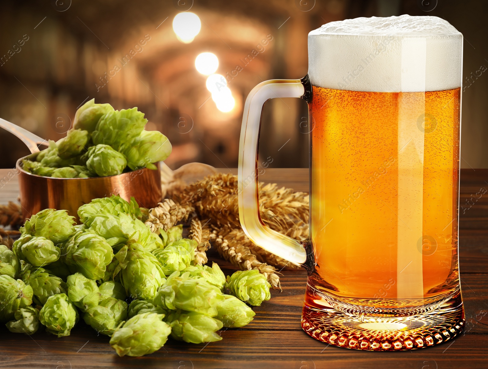 Image of Glass of tasty light beer, fresh hops and wheat spikes on wooden table in cellar