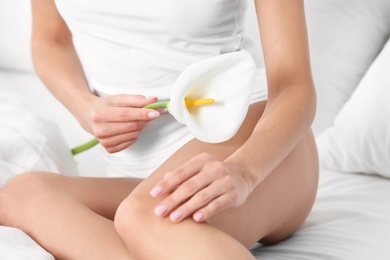 Photo of Young woman with perfect smooth skin holding calla flower on bed, closeup. Beauty and body care