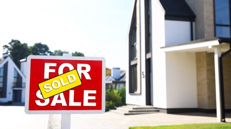 Red real estate sign near house outdoors on sunny day