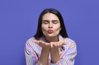 Beautiful young woman blowing kiss on purple background