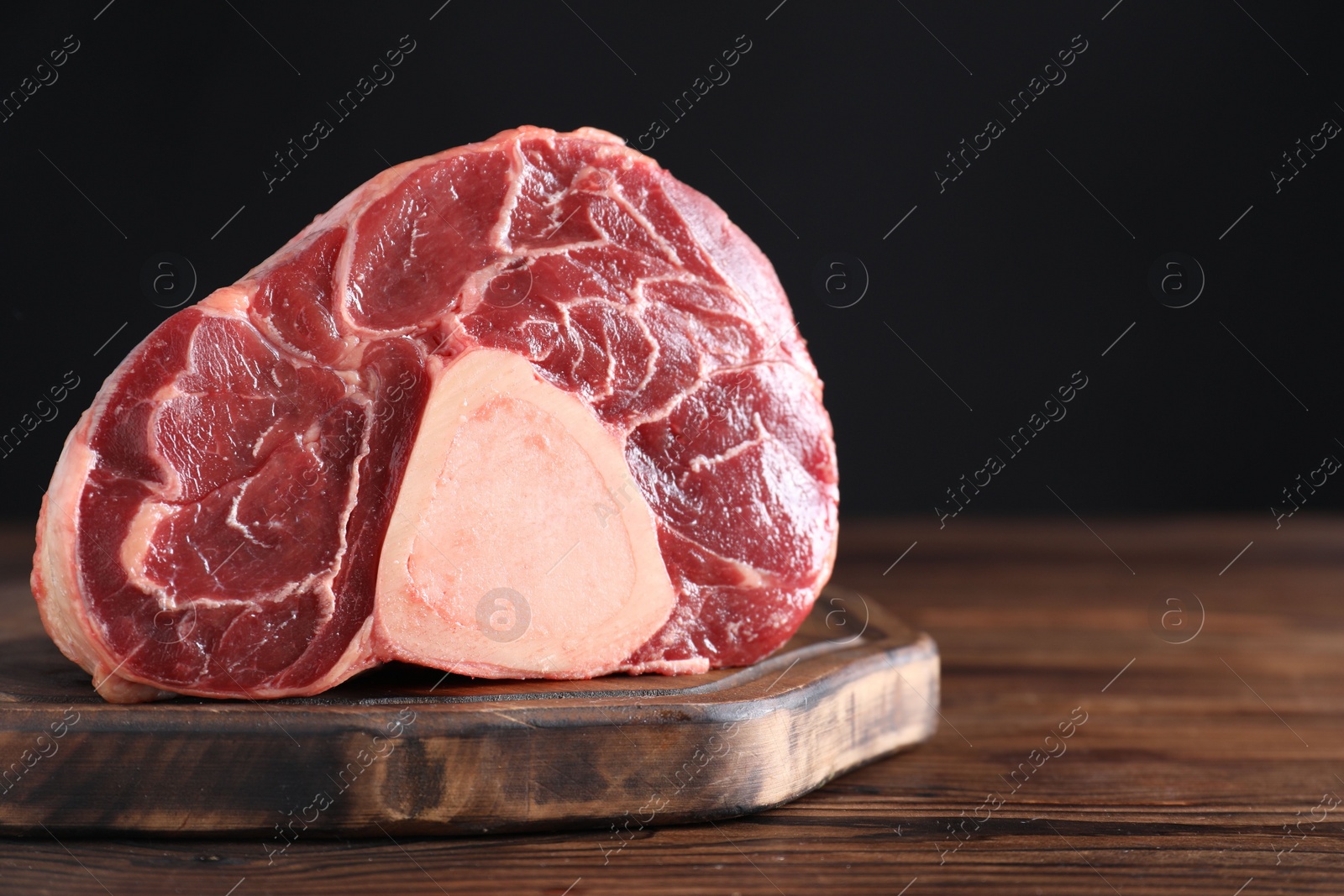Photo of Piece of raw beef meat on wooden table against black background, closeup. Space for text