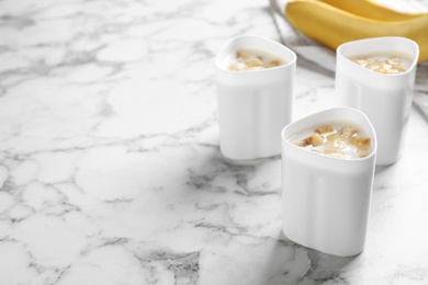 Cups of yogurt with bananas on table, space for text. Multi cooker recipe