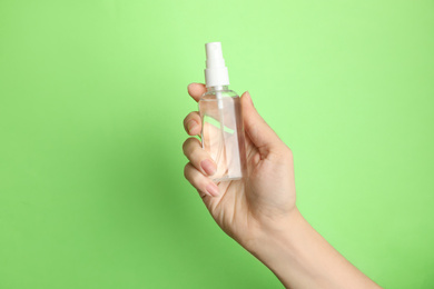 Photo of Woman holding antiseptic spray on green background, closeup