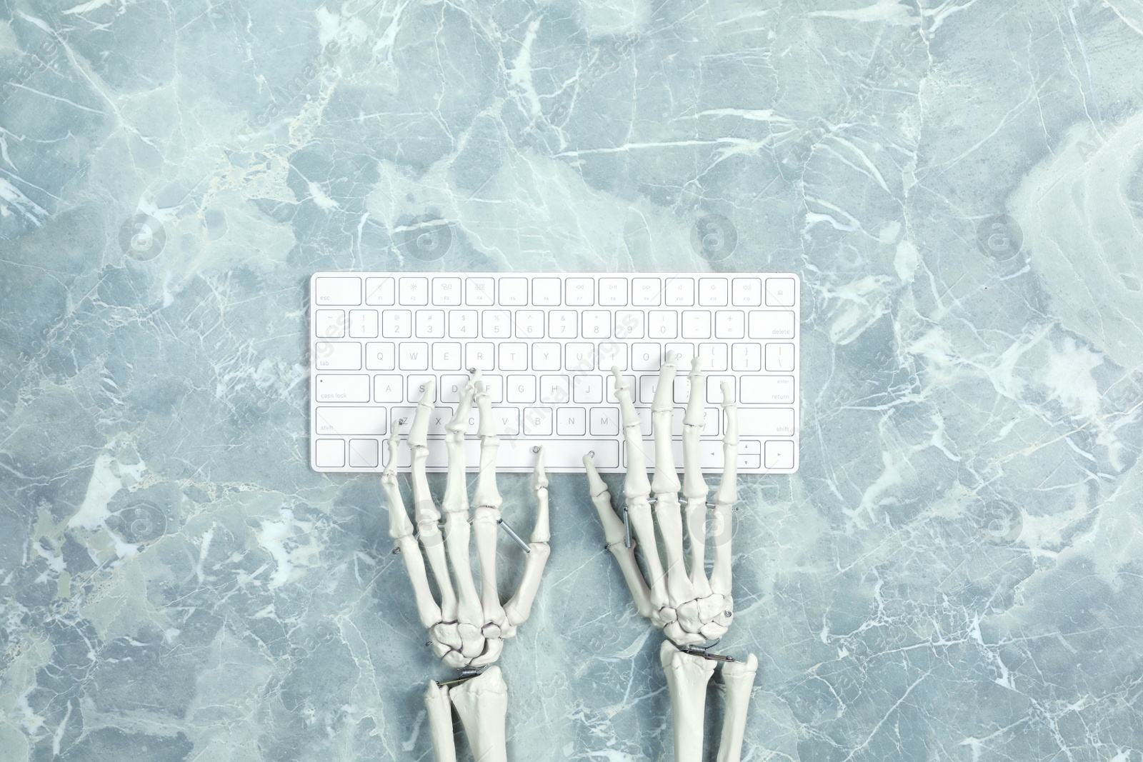 Photo of Human skeleton using computer keyboard at grey marble table, top view