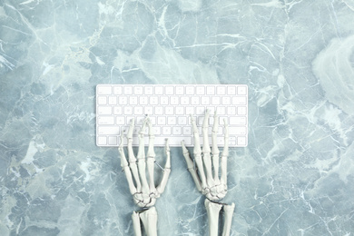 Human skeleton using computer keyboard at grey marble table, top view