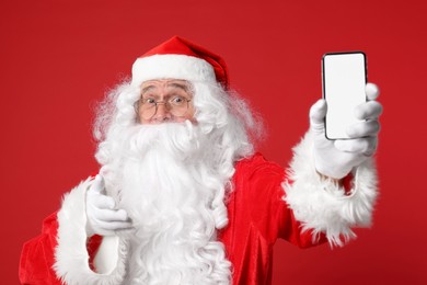 Photo of Merry Christmas. Santa Claus showing smartphone on red background