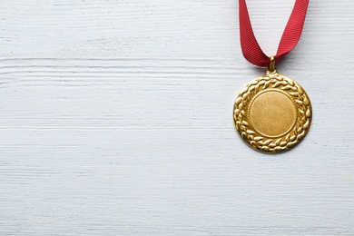 Gold medal with space for design on white wooden background, top view. Victory concept