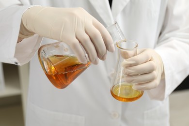 Laboratory worker pouring orange crude oil into flask, closeup