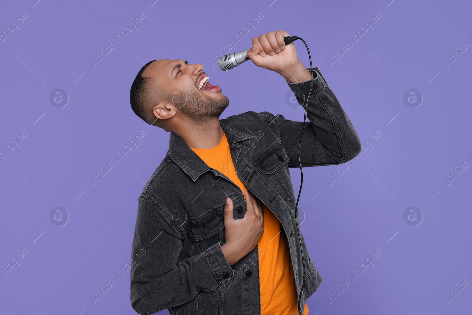 Photo of Handsome man with microphone singing on violet background