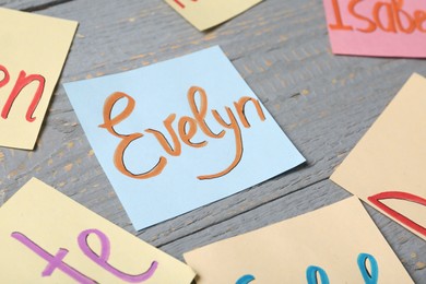 Photo of Paper sheet with written baby name Evelyn on grey wooden table, closeup