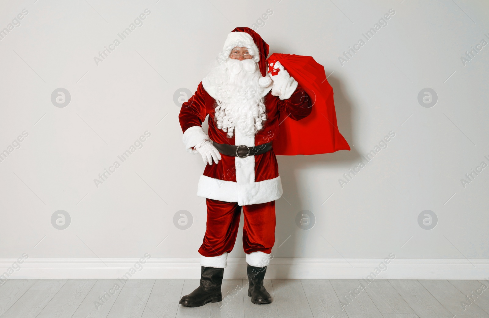 Photo of Authentic Santa Claus with bag full of gifts against grey wall