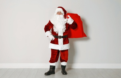 Authentic Santa Claus with bag full of gifts against grey wall