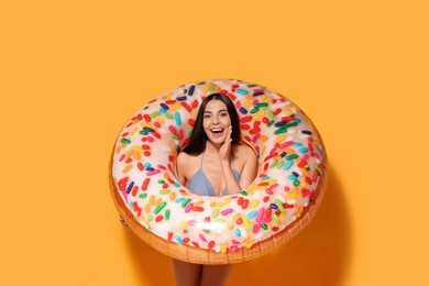 Young woman with inflatable ring against orange background