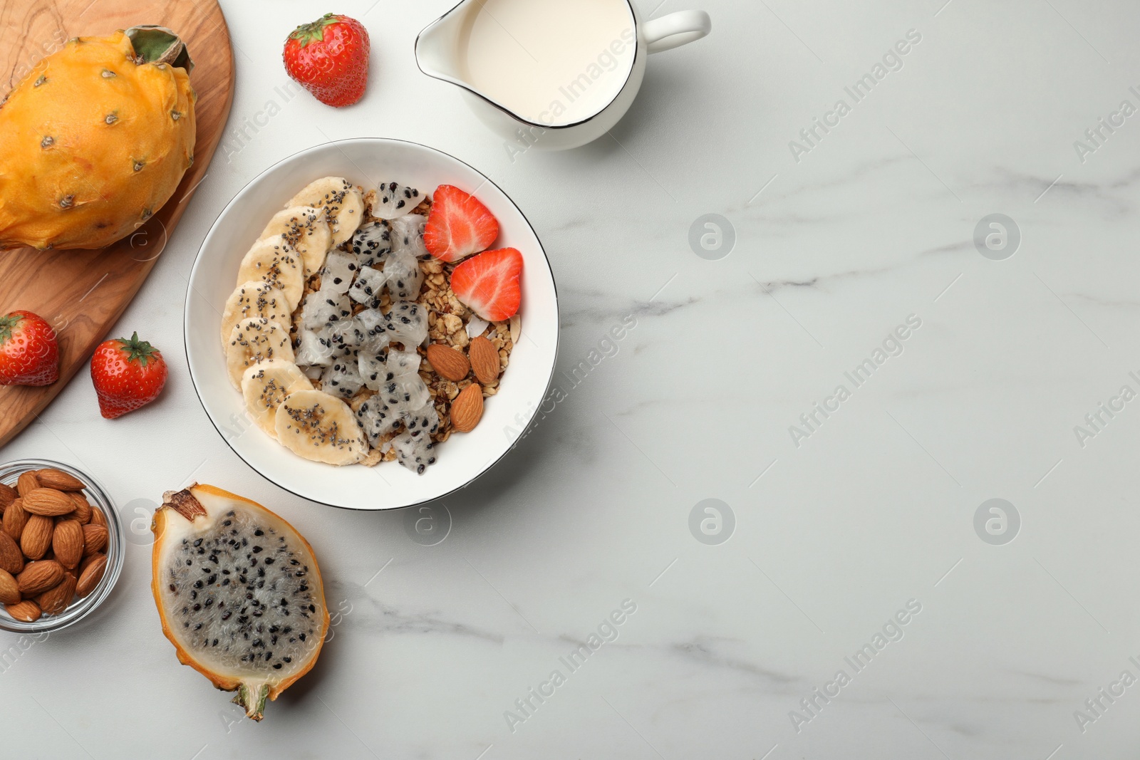 Photo of Bowl of granola with pitahaya, banana and strawberry on white marble table, flat lay. Space for text