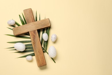 Wooden cross, painted Easter eggs and palm leaf on beige background, flat lay. Space for text