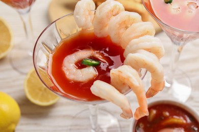 Photo of Tasty shrimp cocktail with sauce in glasses and lemon on light wooden table, closeup