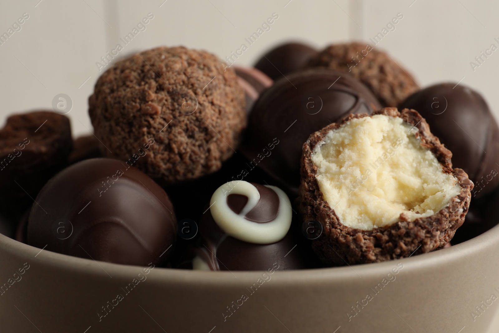 Photo of Many different delicious chocolate truffles in bowl, closeup