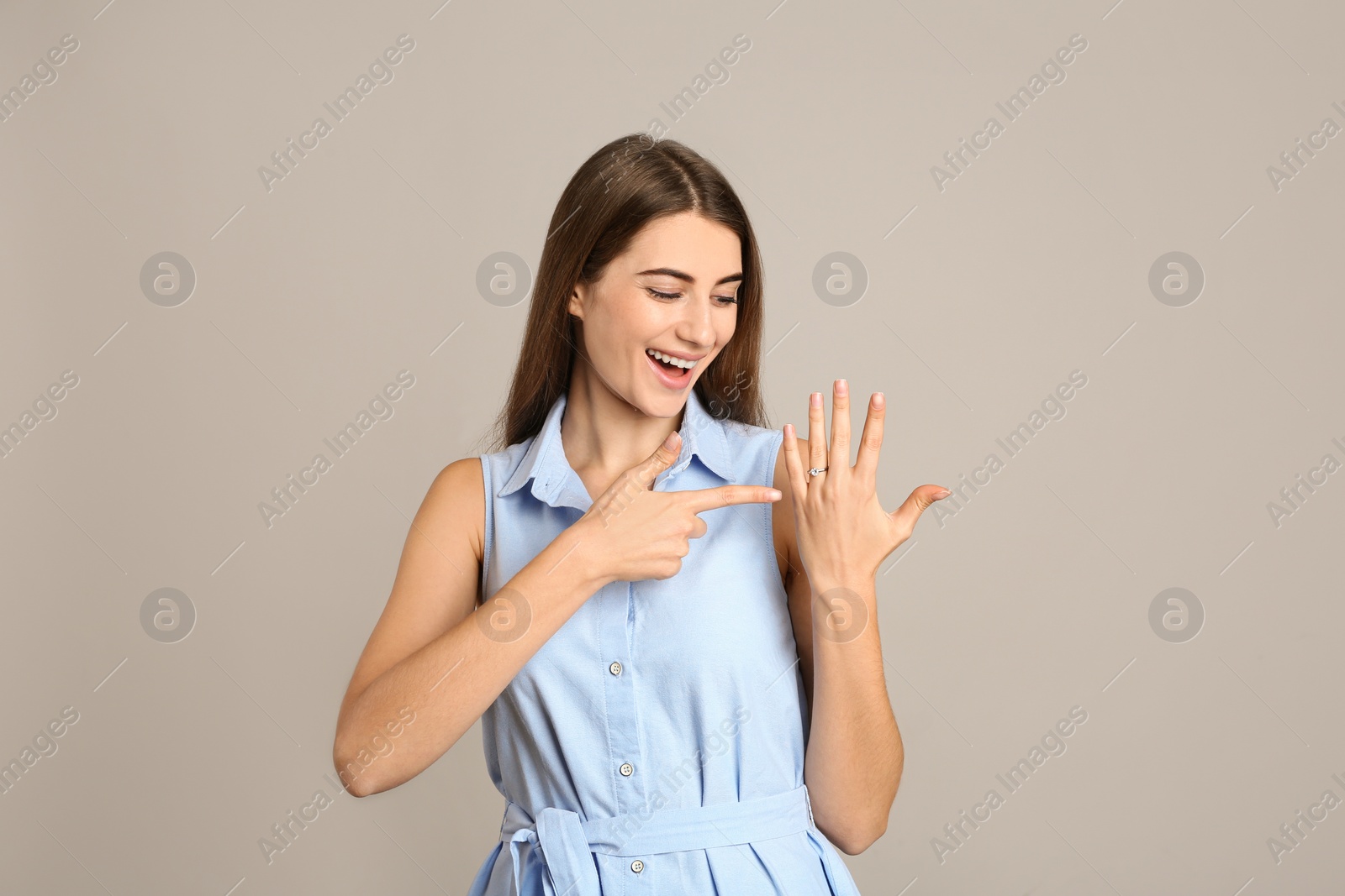 Photo of Happy young woman wearing beautiful engagement ring on grey background