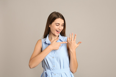 Happy young woman wearing beautiful engagement ring on grey background