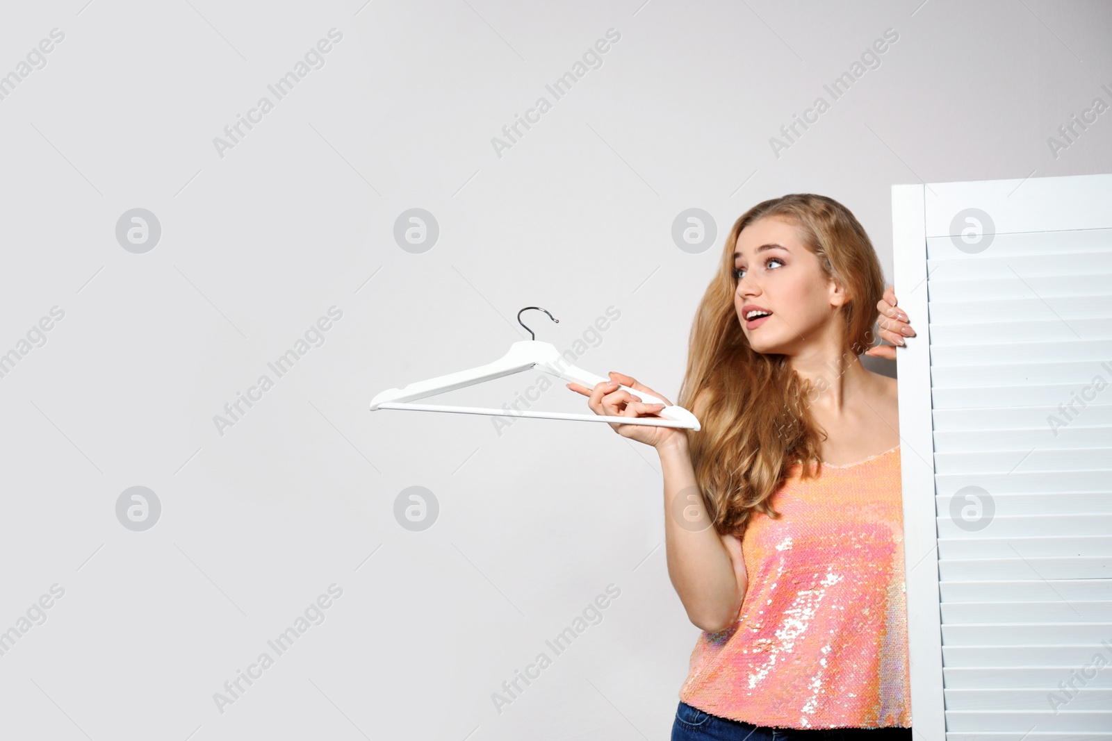 Photo of Young woman with hanger near folding screen against light background, space for text. Dressing room