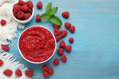 Photo of Raspberry puree in bowl and fresh berries on light blue wooden table, flat lay. Space for text