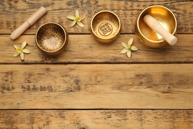 Golden singing bowls, mallets and flowers on wooden table, flat lay. Space for text