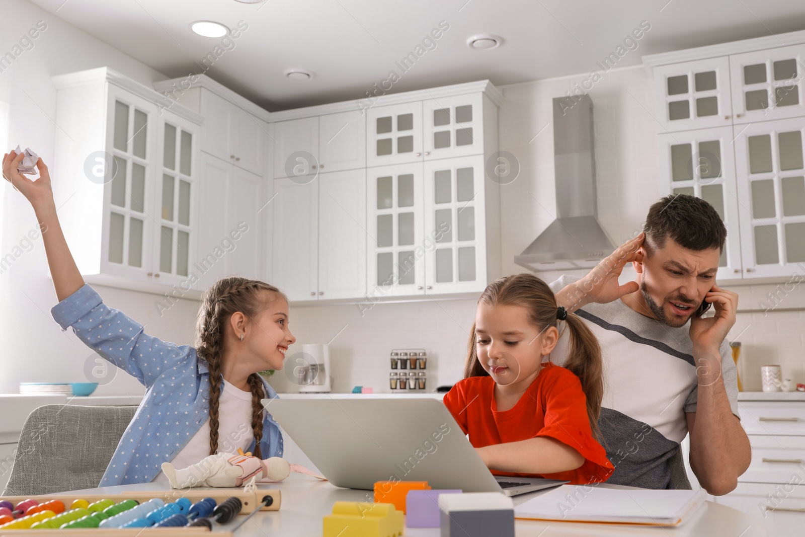 Photo of Children disturbing stressed man in kitchen. Working from home during quarantine