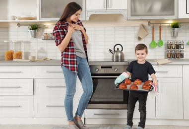 Photo of Cute boy treating mother with oven baked buns in kitchen