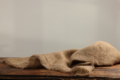 Natural burlap fabric on wooden table against light background. Space for text