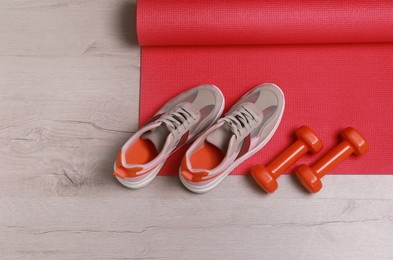 Photo of Dumbbells, sneakers and mat on wooden floor, above view