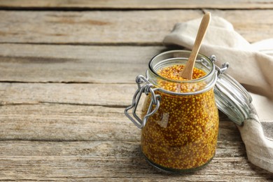 Whole grain mustard and spoon in jar on wooden table. Space for text