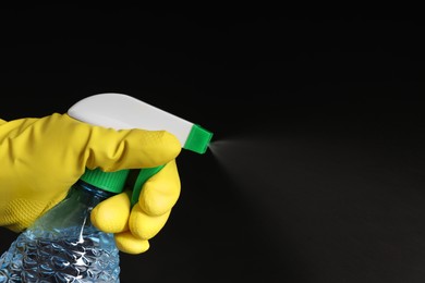 Photo of Woman spraying liquid from bottle on black background, closeup. Space for text