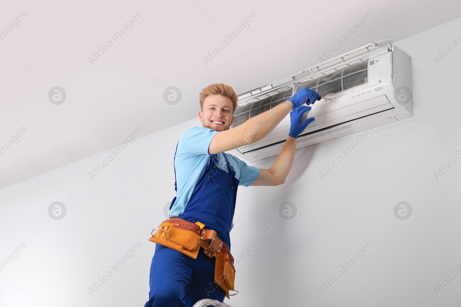 Photo of Professional technician maintaining modern air conditioner indoors