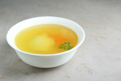 Delicious chicken bouillon with parsley on light grey textured table. Space for text