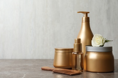 Different hair products, flower and wooden comb on grey table. Space for text