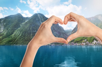 Image of Woman making heart with hands near lake and mountains on sunny day, closeup