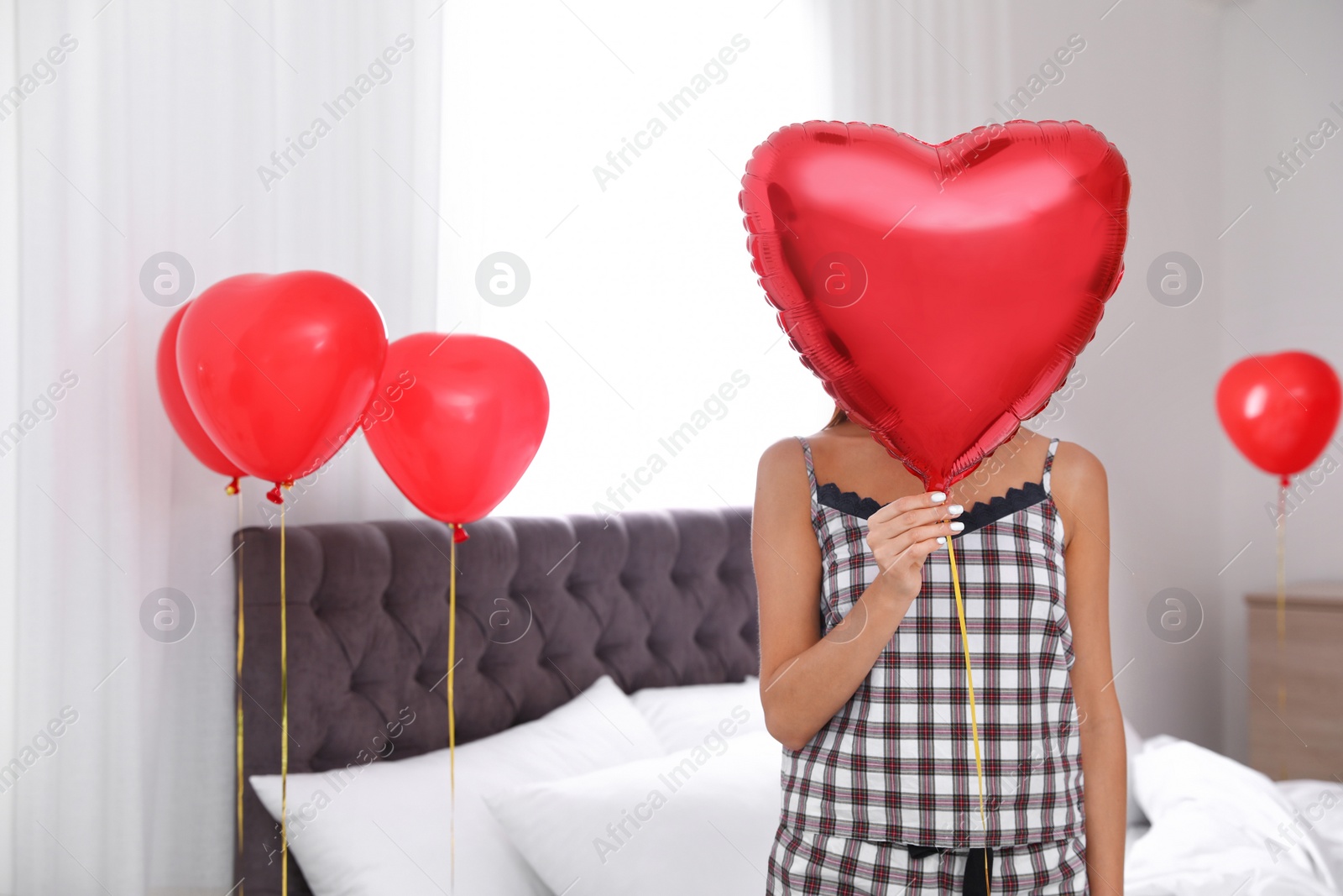 Photo of Young woman in bedroom decorated with air balloons. Celebration of Saint Valentine's Day