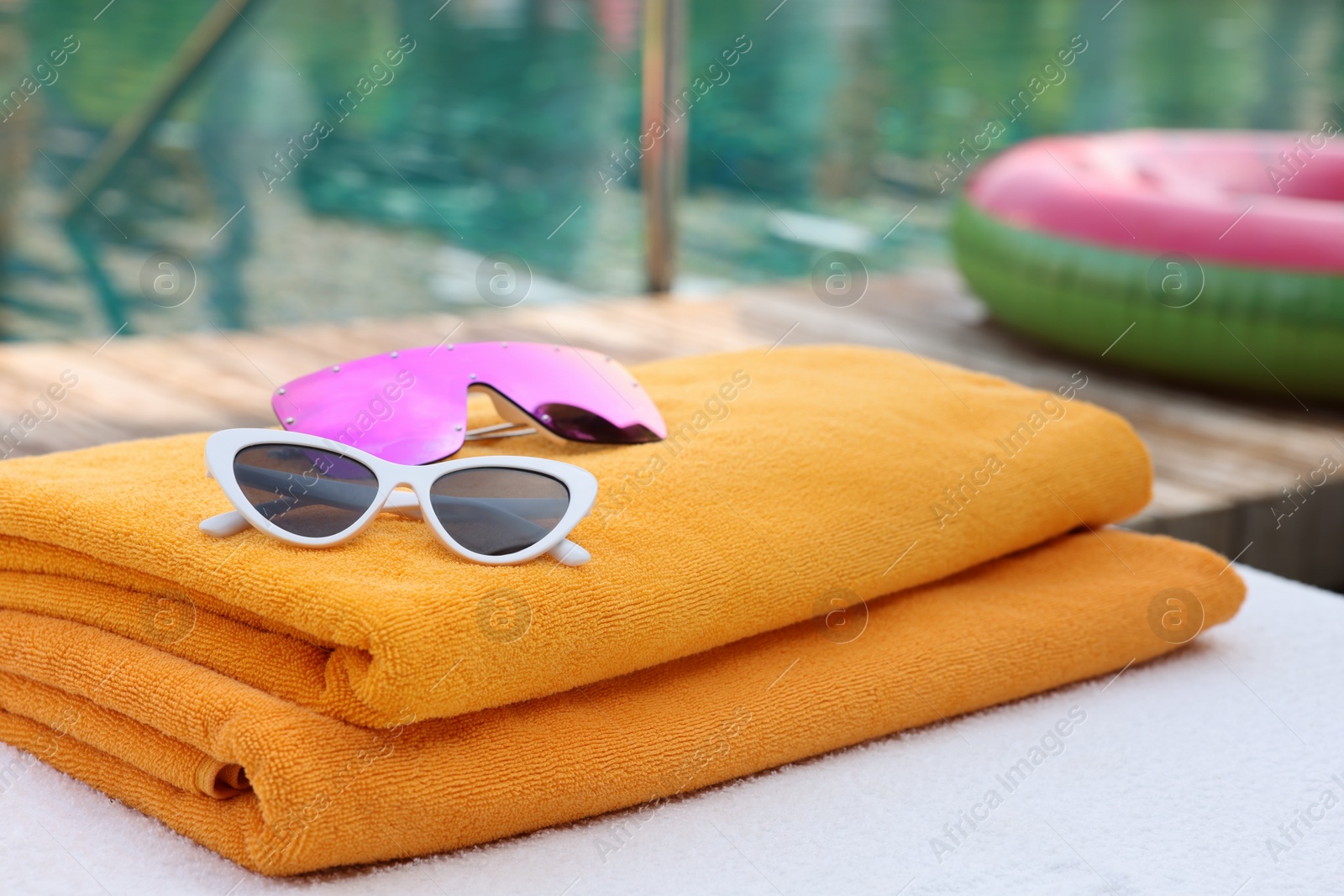 Photo of Beach towels and sunglasses on sun lounger near outdoor swimming pool. Luxury resort