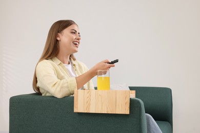 Photo of Happy woman switching TV channels at home. Glass of juice on sofa armrest wooden table
