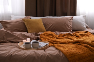 Cups of hot drink and candles on bed with brown linens in room