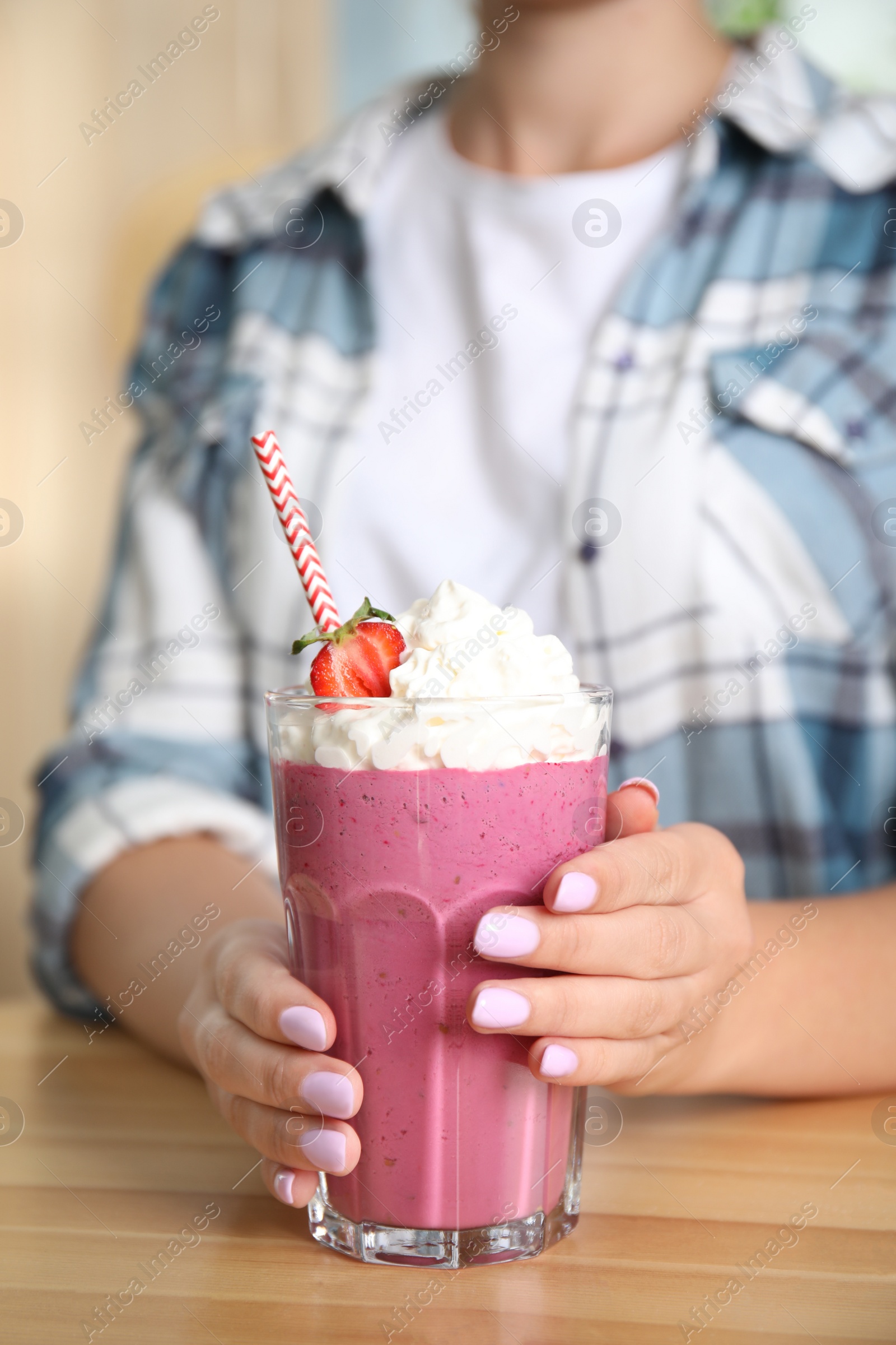 Photo of Woman holding tasty fresh milk shake with strawberry at table indoors, closeup