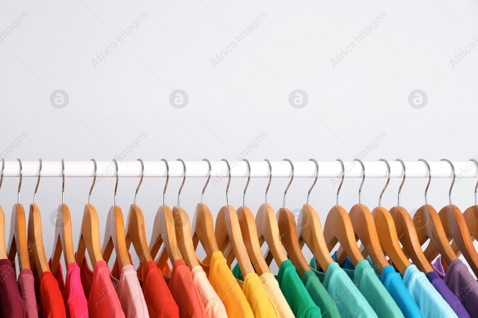 Photo of Rack with rainbow clothes on light background