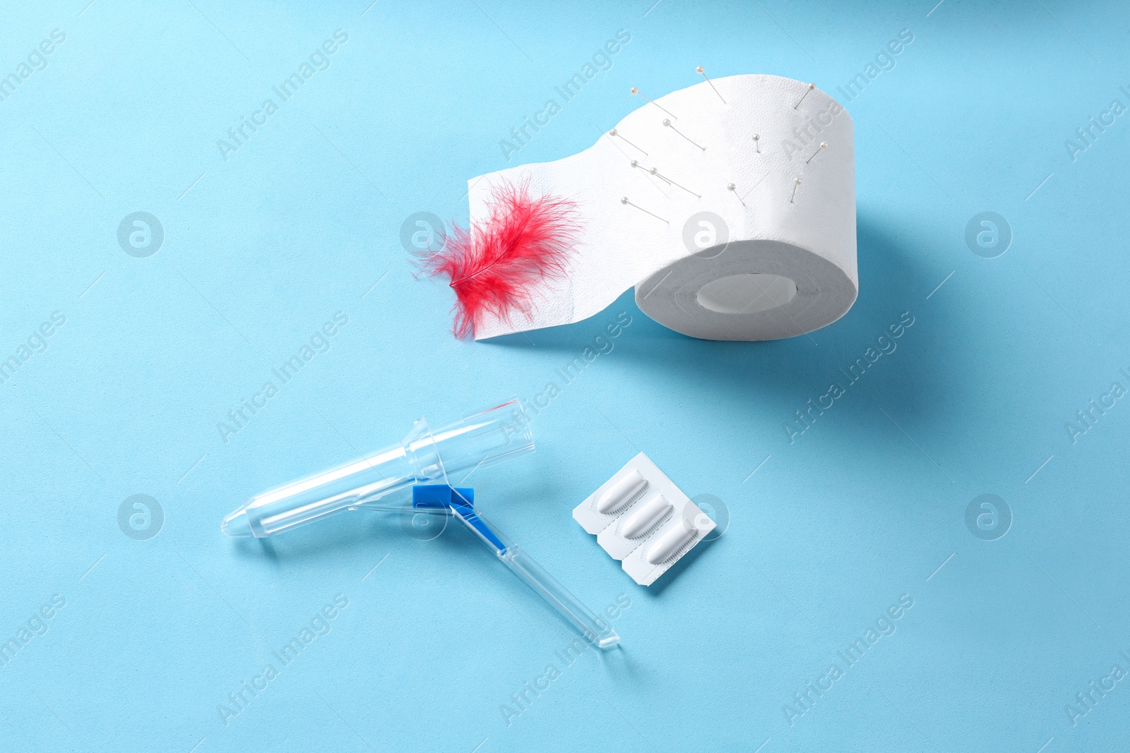 Photo of Anoscope, suppositories and toilet paper with red feather on light blue background, flat lay. Hemorrhoid treatment