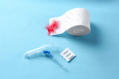 Anoscope, suppositories and toilet paper with red feather on light blue background, flat lay. Hemorrhoid treatment