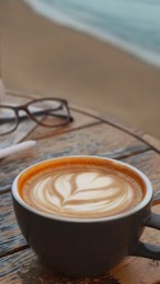 Photo of Cup of delicious coffee, eyeglasses and newspaper on wooden table