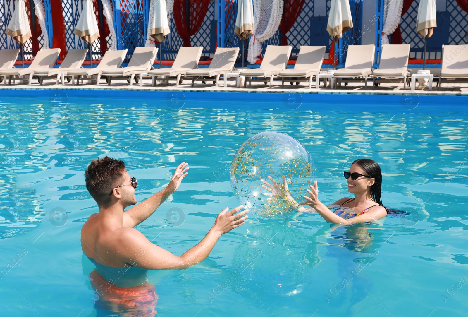 Photo of Woman in bikini and her boyfriend playing with inflatable ball at resort. Happy young couple