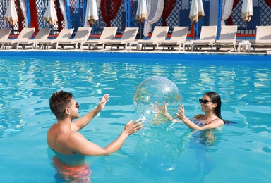 Photo of Woman in bikini and her boyfriend playing with inflatable ball at resort. Happy young couple