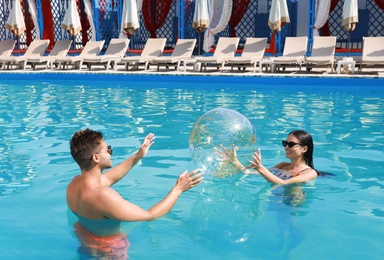 Woman in bikini and her boyfriend playing with inflatable ball at resort. Happy young couple