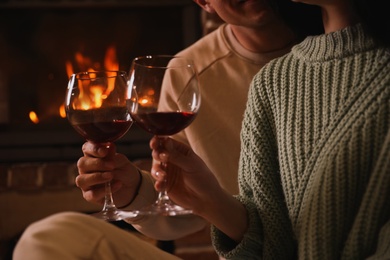 Photo of Couple with glasses of red wine near fireplace, closeup